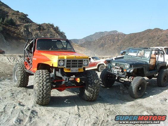 1994 Jeep YJ with custom roll cage and large tires, parked next to another modified Jeep