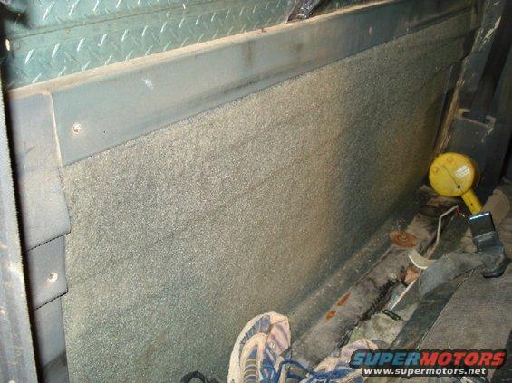 Interior shot of a vehicle showing carpeted wall, metal trim, and a yellow device on the floor