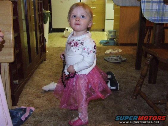 Toddler wearing a pink tutu and holding beads, standing indoors