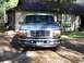 1996 Ford Bronco - A silver 1996 Ford Bronco is parked on a dirt driveway in front of a house.