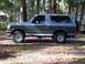 1996 Ford Bronco - This Ford Bronco is parked on a dirt lot surrounded by trees, with a spare tire mounted on the back.