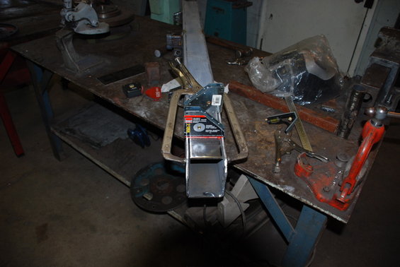 Metal bracket held by large clamps on a workbench with tools