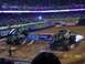 1993 Ford Bronco - Two monster trucks compete in a stadium event, with a crowd watching from the stands.