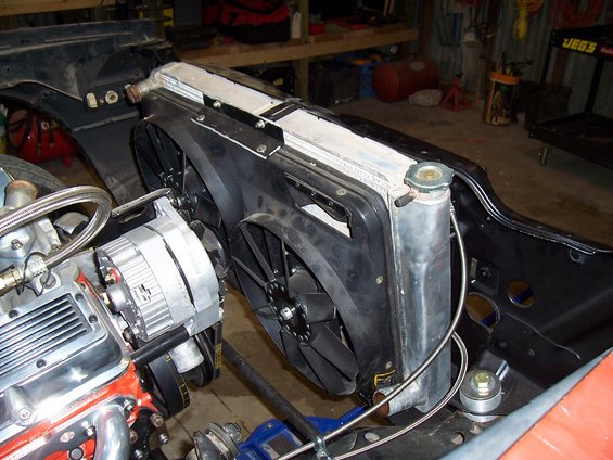Close-up of a car's engine bay showing the radiator, dual electric fans, and alternator