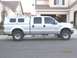 2004 Ford F-250 - Side view of a silver 2004 Ford F-250 Super Duty pickup truck equipped with a camper shell and aftermarket wheels.