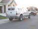 2004 Ford F-250 - A silver pickup truck with a camper shell is parked on the street, with a red pickup truck behind it.