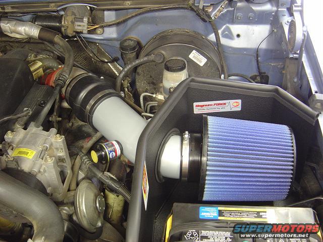 Engine bay with blue K&N air filter and grey intake tube. SuperMotors.net logo visible on battery