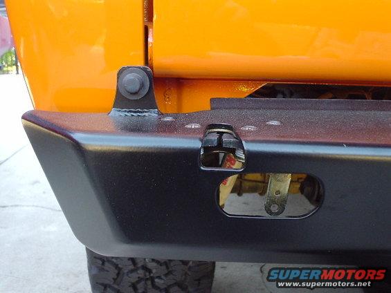 Close-up of an orange vehicle's rear bumper with a black textured finish and a tow hitch receiver