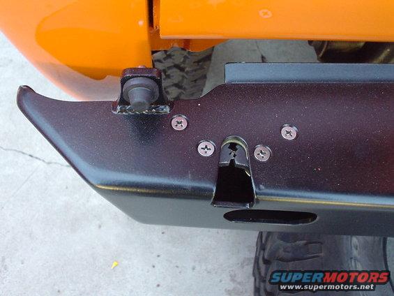 Orange vehicle body panel above black metal bumper with visible mounting hardware and tire tread below