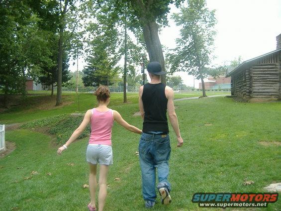 Couple walking away from camera in a grassy park with trees and a log cabin