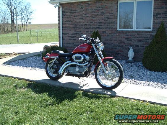 Red Harley-Davidson motorcycle parked on a sidewalk in front of a brick house