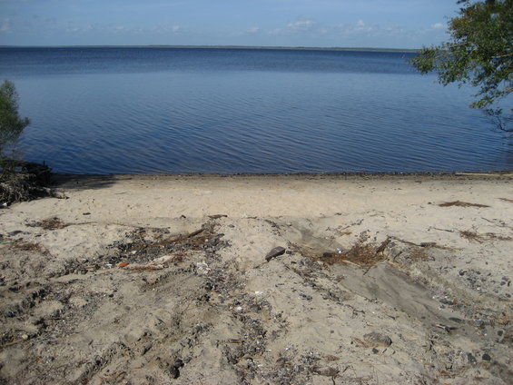 Sandy beach leading to a large body of blue water under a partly cloudy sky