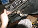 1978 Ford Bronco - A hand manipulates a linkage on a transmission component, with tools and a box of paper visible in the background.