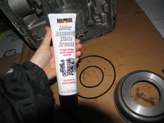 hand holding tube of white grease next to transmission case and seal