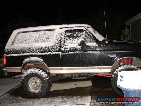 Black 1996 Ford Bronco covered in snow, side view, lifted suspension, tan lower trim