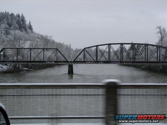 Metal truss bridge over a river with snow-covered trees on the bank