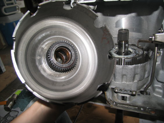 Close-up of a transmission's torque converter and planetary gears. A hand holds the converter, showing its internal splines and bearing
