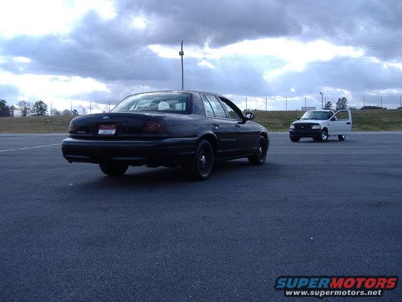 Black 2001 Ford Crown Victoria parked on asphalt, white pickup truck in background with door open