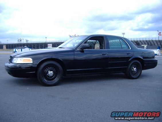 Black 2001 Ford Crown Victoria parked on asphalt with stadium seating in background