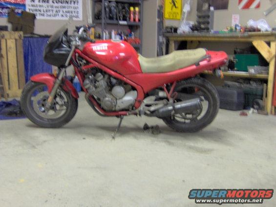 Red Yamaha motorcycle parked in a garage with shelves and tools in the background