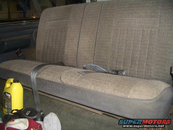 1988 Ford Bronco rear bench seat with seatbelts and a yellow bottle of fluid on the floor