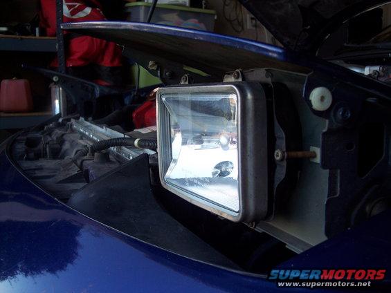 Blue car's front headlight assembly removed, showing internal components and wiring