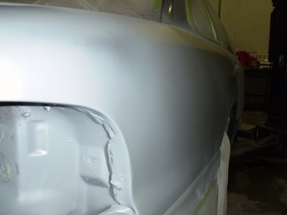 Gray car body panel with primer, showing damage on the lower edge