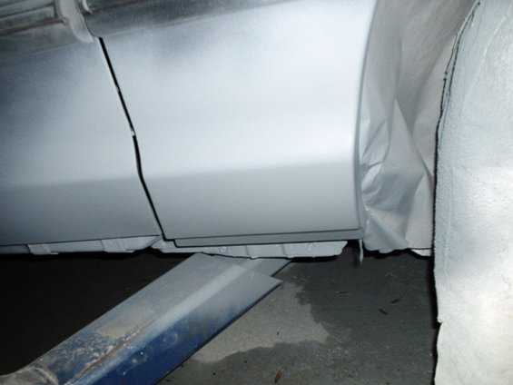 Gray primer on car door seam and rocker panel, covered in protective sheeting