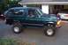1994 Ford Bronco - This lifted 1994 Ford Bronco features a dark green exterior and aftermarket wheels, presented in a three-quarter front side view.
