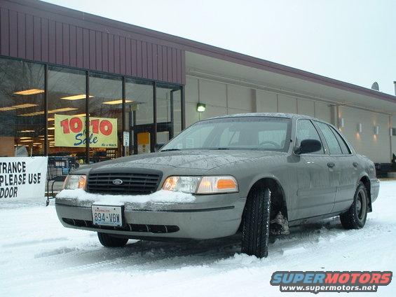 Gray 2000 Ford Crown Victoria parked in snow outside a store with a '10 10 Sale' banner visible through the window