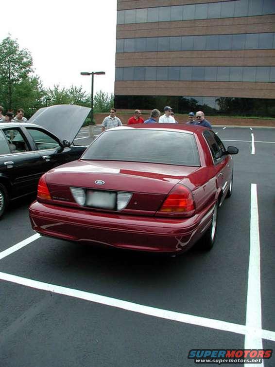 Red sedan parked in a lot, another car with hood up next to it. People standing around