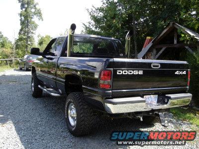 Black Dodge 2500 pickup truck with chrome exhaust stacks, seen from the rear