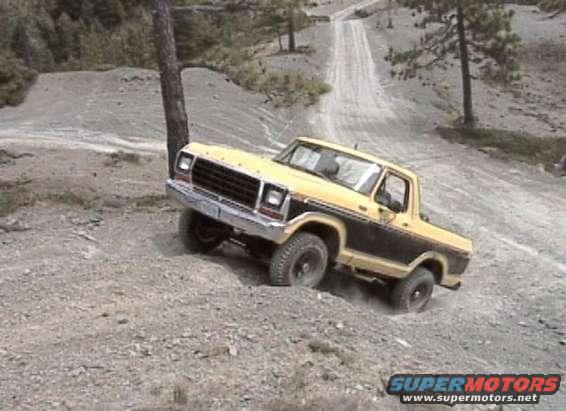 Yellow and black Ford Bronco climbing a dirt hill, front-left wheel elevated