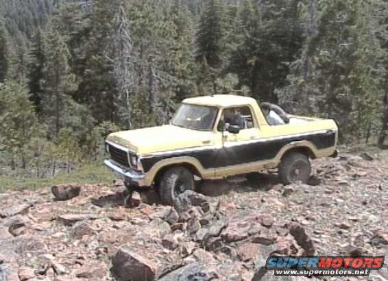 Yellow and black Ford Bronco driving over rocks in a forest