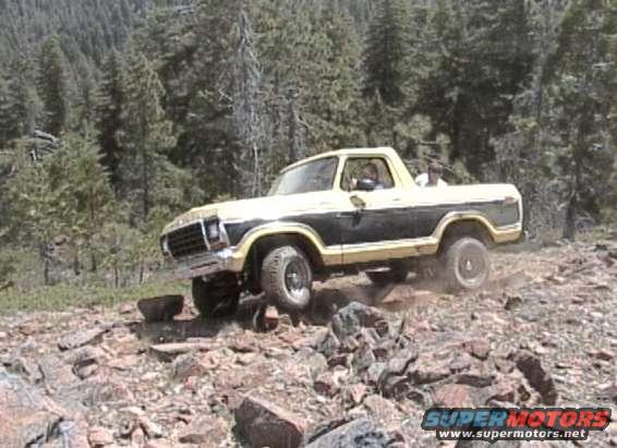 Yellow and black Ford Bronco driving on a rocky, wooded trail