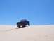 1994 Ford F-150 - A dark blue pickup truck drives up a sand dune under a clear blue sky.
