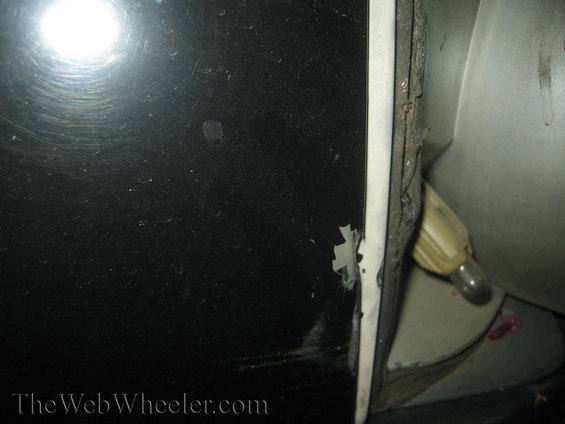 Black car door edge showing chipped paint and a light fixture inside