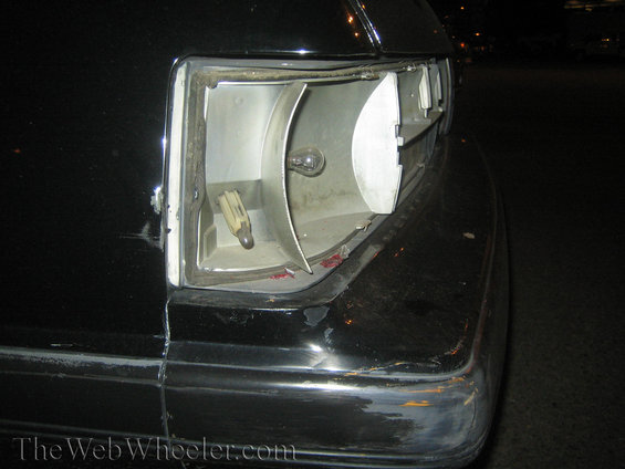 Close-up of a damaged taillight housing on a black car, showing the bulb socket and exposed interior