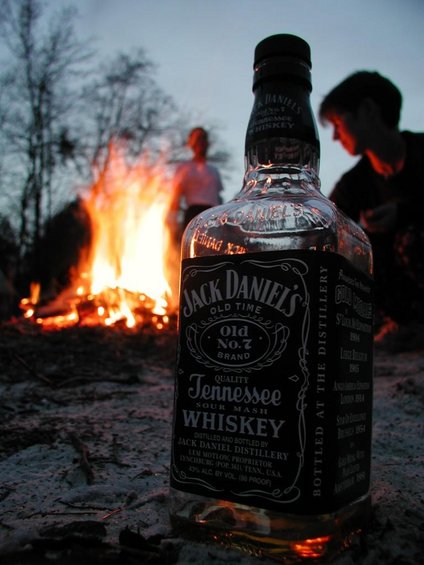 Jack Daniel's bottle in front of campfire with people in background