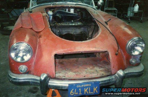 Front view of a red 1959 MG A with hood open, sitting on jack stands