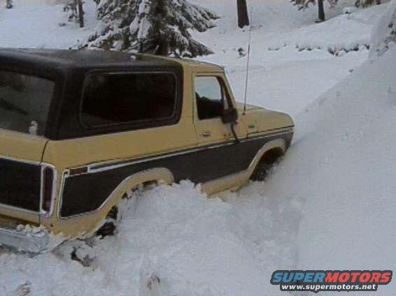 Yellow and black 1978 Ford Bronco stuck in deep snow, front-right wheel visible