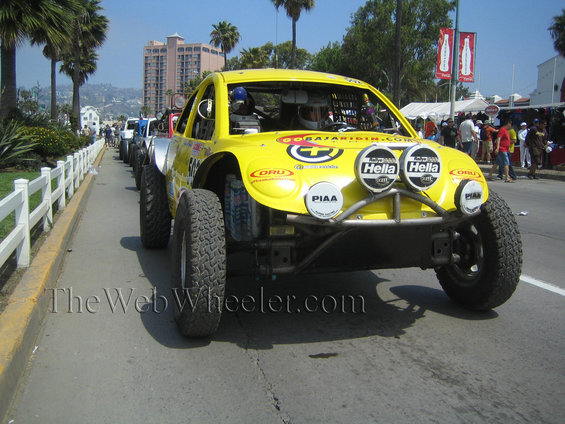 Yellow off-road racing car with large tires and multiple lights, parked in a line with other vehicles