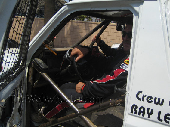 Driver and co-driver in a race truck, wearing racing suits. Roll cage visible