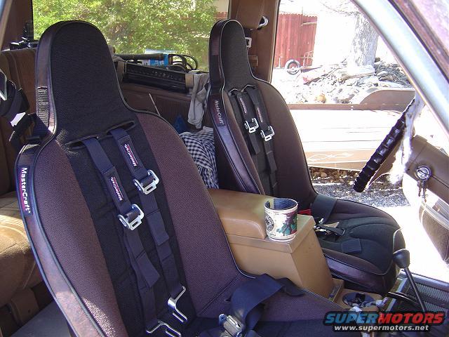 Vehicle interior with two bucket seats, racing harnesses, and a cup holder