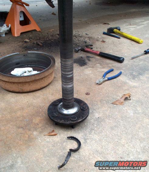 Axle shaft with hub and brake drum on concrete, tools scattered around