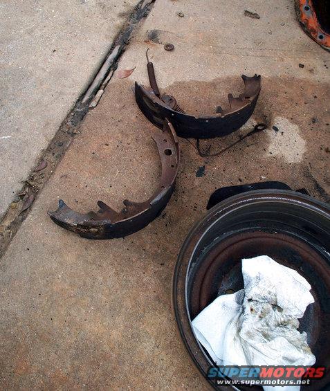 Drum brake parts on concrete, including two brake shoes and a drum with a dirty paper towel inside
