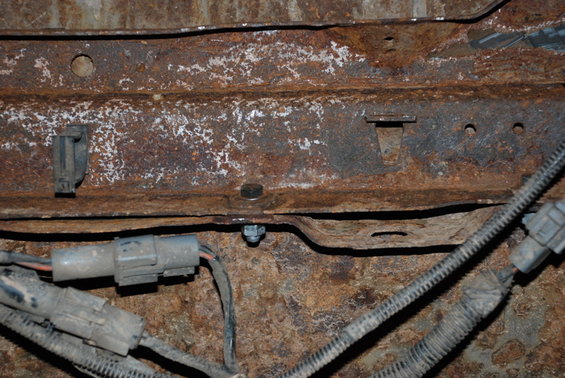 Heavily rusted metal frame section with two grey electrical connectors and wiring harnesses