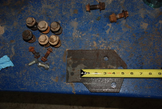metal bracket with two holes, measured with a tape measure, next to several bolts and nuts on a blue surface