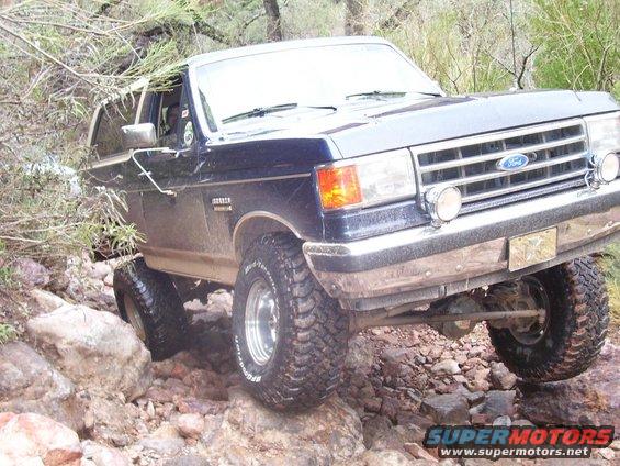 Dark blue Ford Bronco off-roading over rocks, front 3/4 view