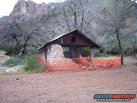 Abandoned stone and wood structure with orange safety netting in a rocky, arid landscape